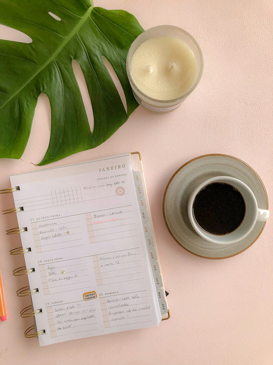 a cup of coffee next to a planner and a candle